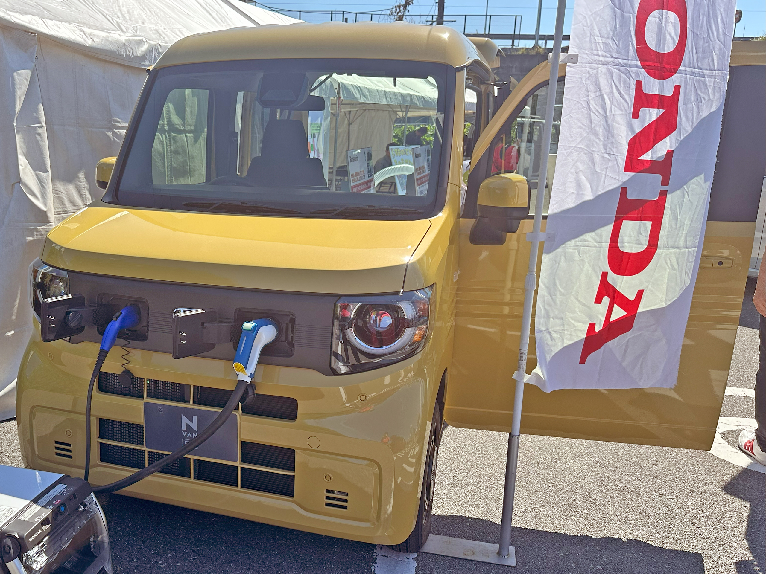 2024年10月14日撮影のN-VAN e: FUN前部。充電口と外部給電の展示接続。日本向け展示車の参考写真で、購入対象の装備とは異なる場合があります。